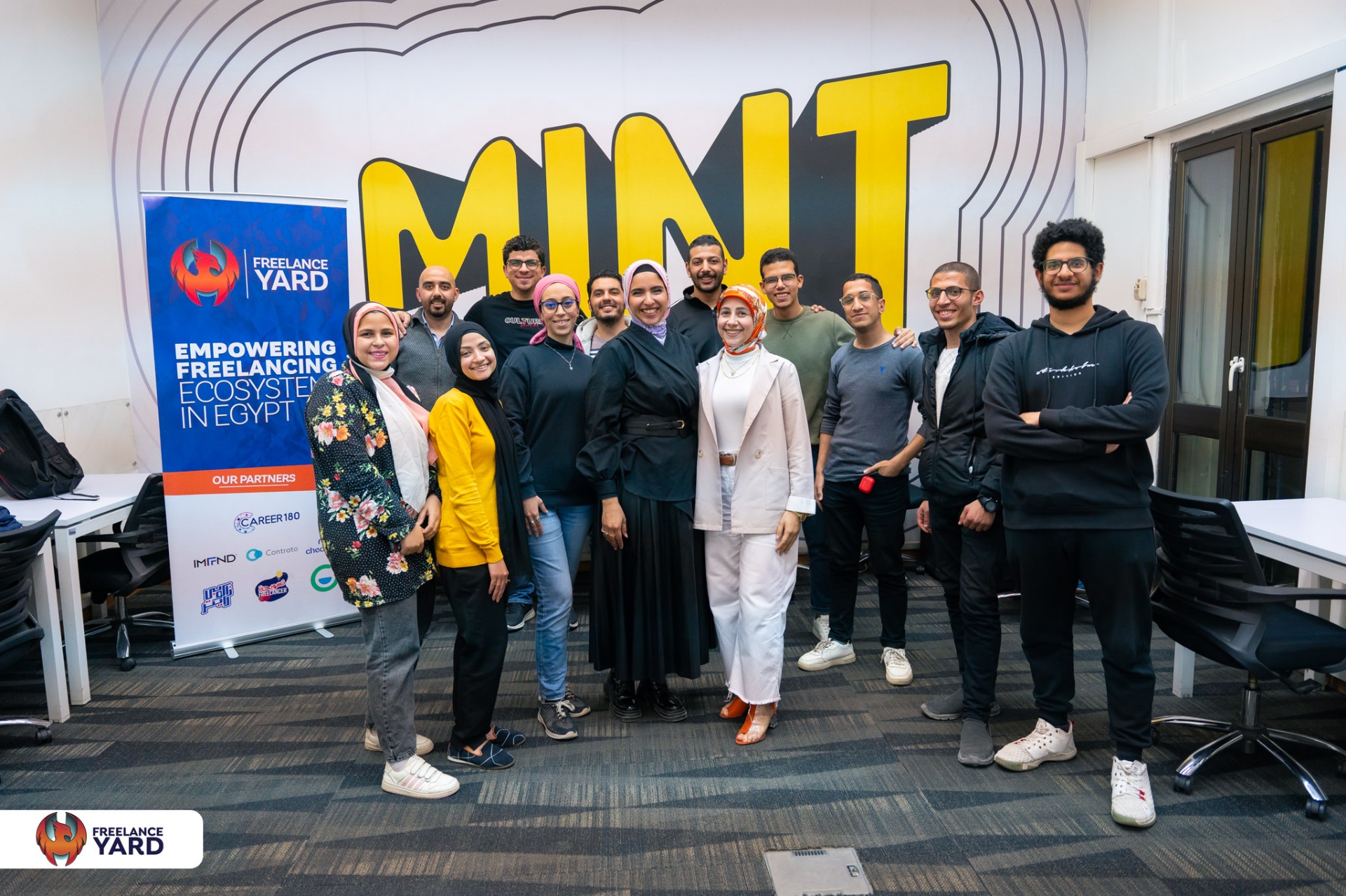 Alaa El Emam standing with a group of participants in front of a MINT wall sign at Freelance Yard